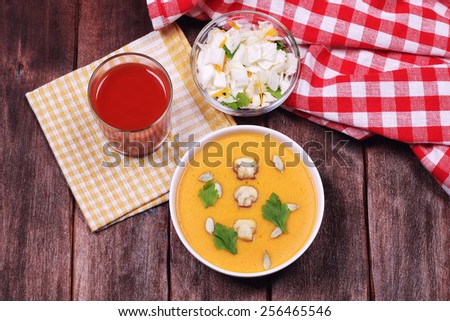 A bowl of vegetable soup puree on the table. A bowl of soup, a glass of tomato juice and a bowl of salad from Chinese cabbage. Vegetarian diet food. Light vegetable dinner. Home-cooked meal.