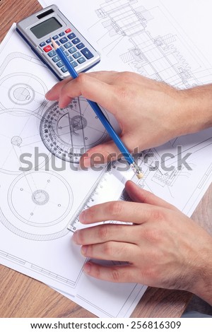 Hands male engineer next to the drawings, a calculator and a protractor. Complex engineering drawings. Workplace mechanical engineer. Students of technical school. The practical work of the student.