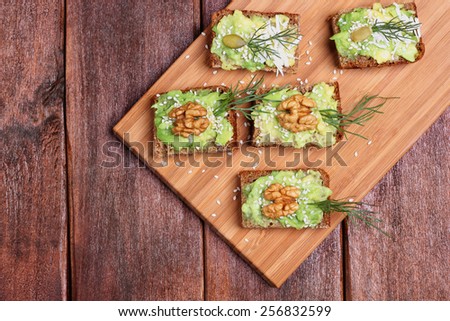 Canapes with paste of avocado, walnuts, cheese and sesame seeds. The concept of the restaurant, a healthy diet food. Snack of canapes with avocado, nuts and herbs on a kitchen board.