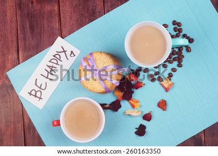 Two cups of coffee on the table. Cookies, rose petals, coffee beans and a cup on the table. Coffee with milk on the table. Morning coffee for two. Top view. Be happy. Cheerful romantic morning.