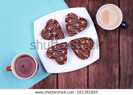 Cup of coffee with milk and cup of tea on the table. Cakes and two cups on the table. Restaurant, coffee shop. He and she, feelings and love. Black tea and coffee latte. Cakes in the shape of hearts.