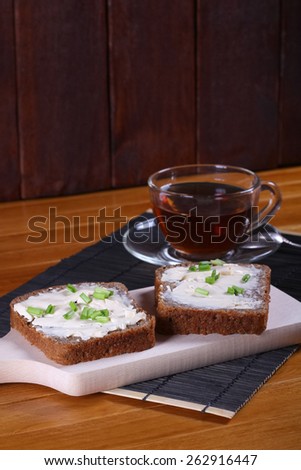 Cup of black tea and sandwiches on the table. Transparent cup of tea. Two sandwiches with butter or cream cheese and chives. Snack, breakfast, lunch.
