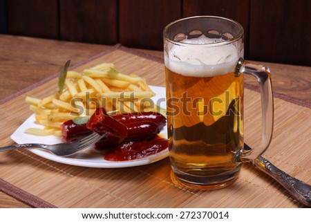 Beer glass and plate of food. The Friday evening. Mug of beer on the table. A light beer. Meat, potatoes and beer. Potatoes deep-fried, sausages, ketchup and beer.