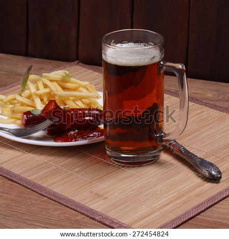 Beer glass with dark beer on the table. Unhealthy food. A hearty lunch. Beer, fried potatoes, sausage and ketchup on the table. Ordering food in a pub.
