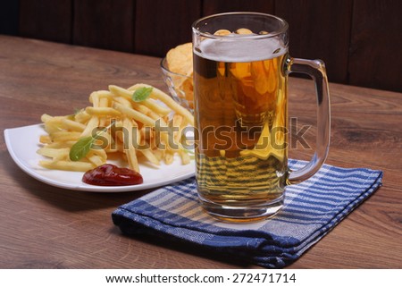 Beer glass and plate of food. Mug of beer on the table. Junk food. Relax with a beer. A light beer. Potatoes and beer. Fries potatoes, ketchup, chips and beer. The Friday evening.