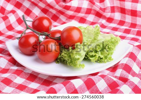 Vegetables on a square plate. Red tomatoes on a branch, lettuce. Organic vegetables. The cherry tomatoes on a branch. Ingredients for cooking.  Tomatoes and leafy green lettuce.