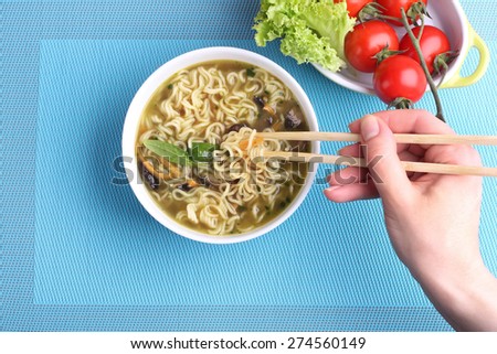 Hand with Chinese chopsticks.  Chinese noodles in soup. Soup with noodles and mushrooms. The seafood chowder. Kitchen Asia. The vegetables on the plate. Tomatoes on the branch and lettuce.