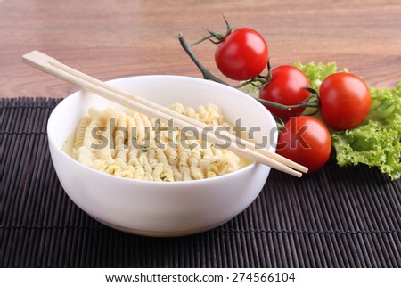 Noodles in the bowl. Bowl, noodles and broth. Vegetables on the table. Tomato and lettuce. Chinese instant noodles. Chopsticks and noodles. Kitchen Asia. The view from the top. The food in the plate.