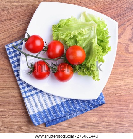 Vegetables on a square plate. Red tomatoes on a branch, lettuce. Organic vegetables. The cherry tomatoes on a branch. Top view. Lunch on the plate. Vegetarianism, raw food diet.