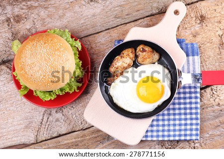 Roll with sesame and vegetables. A wooden table. Fried egg on the pan and meat. The Burger on the plate. Sandwich. White fresh bread, and vegetables.