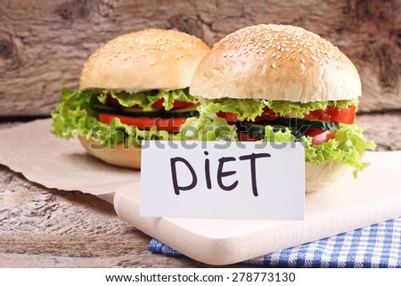 Diet rich breakfast. Diet rolls with sesame and vegetables. Two Burgers on the table. The Burger on the plate. Sandwich. Lettuce, tomato and cucumber. White fresh bread, and vegetables. Wooden table.