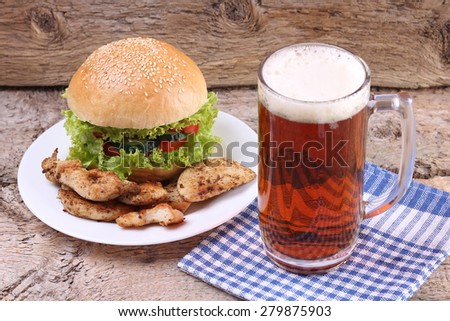 Glass of dark beer and Burger. A plate with Burger and glass of beer. Food and Beer. Lettuce, cucumber, tomato, bread and beer.  Meat and Beer. Serving food on the table. Order meals. Lunch time.