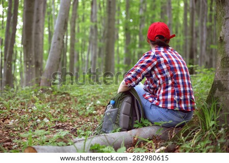 Girl tourist. The tourist is at rest. To relax in nature. Girl in a shirt and a cap with a travel backpack near a tree. Beech forest. The tourist is at rest. A tourist on holiday. A healthy lifestyle.