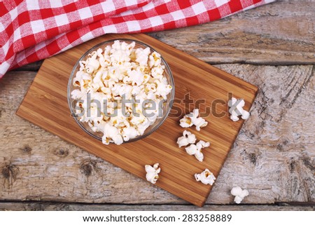 A cutting Board, a bowl of popcorn, towel and scattered popcorn. A bowl of popcorn on the table.Delicious movie snack. Mouth-watering classic appetizer. A lot of popcorn on the table. Top view.