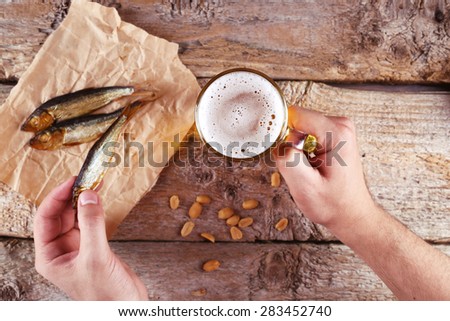 Food and Drink. Light beer and smoked fish on the table. Male hands with a glass of beer and fish. Fish on a crumpled piece of paper. Peanuts, dried fish and beer. A man with a beer and a snack.