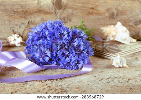 Bouquet of cornflowers on the table. Cornflowers, satin tape, Notepad and shells. Blue flowers. Gift, surprise, and romance. Summer vacation. A lot of flowers. To give the bouquet. Vintage.