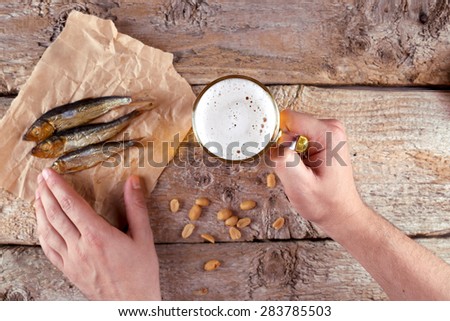 Food and Drink. Light beer and smoked fish on the table. Male hands with a glass of beer and fish. Fish on a crumpled piece of paper. Peanuts, dried fish and beer.