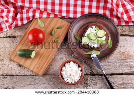 A sandwich with cheese and herbs. Cucumber, lettuce, arugula and cheese. Cooking. Tomato, cucumber and a sandwich. Kitchen Board and a clay saucer. Tasty and low calorie snack.