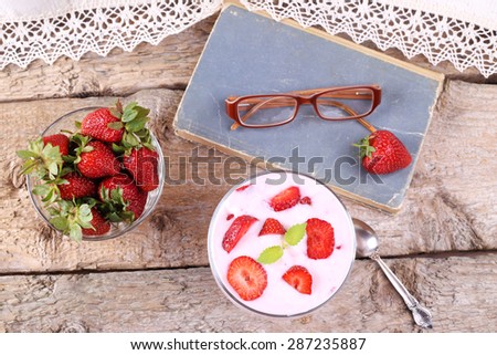 Home-like atmosphere. Strawberry dessert with yogurt. Top view. Strawberry yogurt. The book, eyeglasses, a bowl of strawberries and strawberry dessert. Still life. Rural. Vintage style.