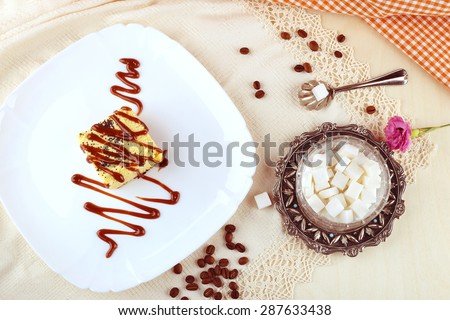 Cheese dessert. Delicious cheesecake and caramel. Caramel sauce on the cake. Baking, dessert, confectionery. Lace tablecloth, sugar bowl with spoon, coffee beans and a sweet dessert.
