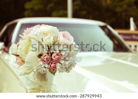 A bouquet of artificial flowers on the car. The wedding procession. Machine for bride and groom. White luxury car with the wedding decorations. Decorate the car. Toned image. Vintage.