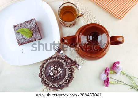 Cup of black tea, tea pot, sweet dessert, sugar bowl and flowers. A gourmet Breakfast. To drink tea. Tea Party. Ceramic teapot, glass with tea and cake on the table. Brownie in powdered sugar.