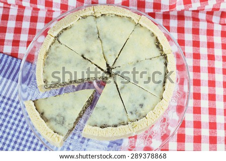 Cake on a platter. Quiche with spinach and vegetables. Cheese cake with filling. Shortbread dough. Restaurant, catering. Vegetable quiche with cheese. Checkered tablecloth, towel, dish and quiche.