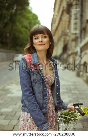 Girl with retro Bicycle in the city. Cyclist on the street. Girl-hipster. Beautiful girl in a summer dress on the street. Smiling girl. Retro Bicycle with basket and flowers, girl next to the bike.
