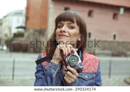 Beautiful young woman with a camera. Street portrait of a smiling girl. Beautiful girl in the denim jacket on the street. Girl photographer. Fashion beautiful girl. Fashionista. Art profession.