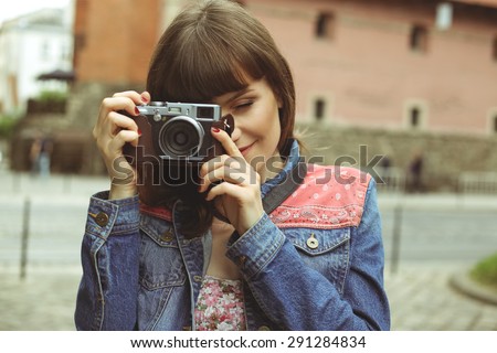 Beautiful young woman. A young woman with a camera . The girl - photographer in the city. Young woman on the streets of the old town . Hipster girl . Vintage look. Retro look. Woman\'s portrait.