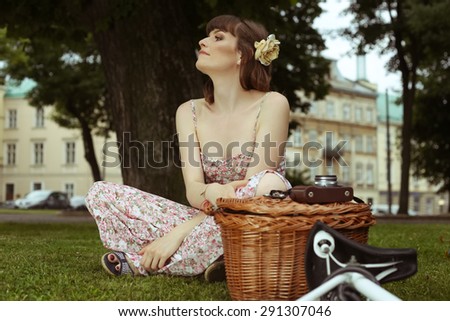 Girl with a flower in her hair. Portrait of a beautiful woman. Cyclist, city bike. Rest on a lawn. Sitting girl. Girl in dress. Attractive woman. Woman\'s portrait. Retro look. Toned image.