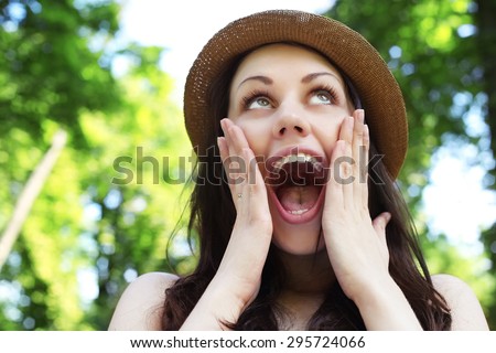 Surprised woman, delight, joy. Portrait of a woman on the street. Joy, positive emotions. Happy face. Open mouth. A woman in a hat. Green trees, summer, park.