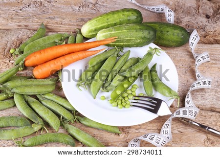 Vegetables on a plate. Vegetable diet. Green vegetables and carrots. Green peas in pods, carrots and cucumbers. Measuring tape and vegetables. Plate with vegetables on the table. Diet concept.