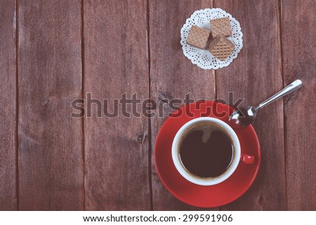Chocolate wafers and cup of black coffee. Strong black coffee in a red cup and sweets. Space for text. Banner. Wooden table. Cup of coffee and waffles on a wooden table.