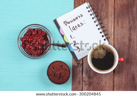 A cup of black coffee and a chocolate muffin and a notebook on the table. Business, brainstorming. Business ideas, business ideas, coming up with ideas. Cherry jam, pastries and coffee. Cheer.