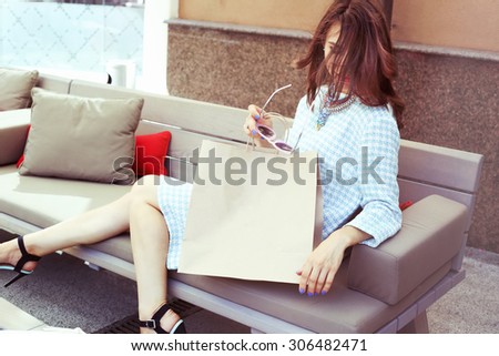 Beautiful glamorous girl in a dress with a paper sack. Rest after shopping. Luxury girl in a checkered dress. Space for text. Girl with sunglasses. Fashion & Style. Stylish Girl.