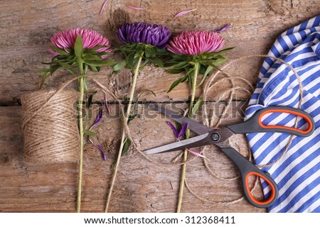 Table of florist. Florist workspace. Scissors, skein harness, three flowers and towel on the table. Old wooden table. The working surface. Make a bouquet. Hobbies, business, occupation.