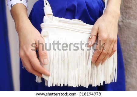Hands and white bag with fringe. White bag with fringe. Accessories. Fashion handbags. Tanned hands. A young woman, girl. Hands-on bag. The blue skirt and white bag.