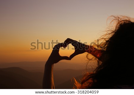 Heart shape. Mountain tourism. Symbol of love. The manifestation of love. Expression of feelings. Love of nature. Girl on a background of mountains. Love and feelings. Wind blowing through her hair.