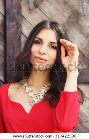 Impressive young girl in a red dress. Girl brunette in a necklace and dress. Brown-eyed brunette. Straightens the hair. Street portrait. Sexy brunette. Bright red dress. Sunny day. Gypsy girl