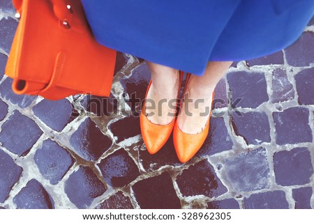 Women\'s legs in orange shoes. Bright orange shoes and bag. Blue coat, orange classic ladies shoes and tote bag. Rainy day. Street fashion. Street style. Business casual look. Autumn outfit.