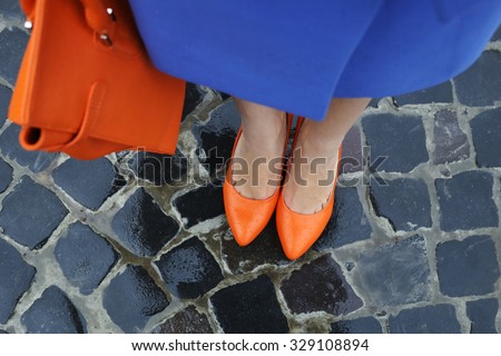 Women\'s legs in orange shoes. Bright orange shoes and bag. Blue coat, orange classic ladies shoes and tote bag. Rainy day. Street fashion. Street style. Business casual look. Autumn outfit.