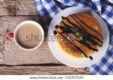 Serve pancakes and a cup of latte on a table. Coffee with milk in a mug. Cup of coffee and dessert. Pancakes with chocolate sauce and mint leaves. Dough. Products from the test. Pancakes recipe.