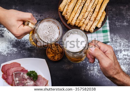 Plate with meat, salted peanuts and cheese sticks to beer. Two glasses with light beer in male hands, drinking in the pub with a friend.