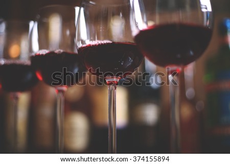 Row of elegant wine glasses with red wine on the bar on the background of a row of alcohol bottles.