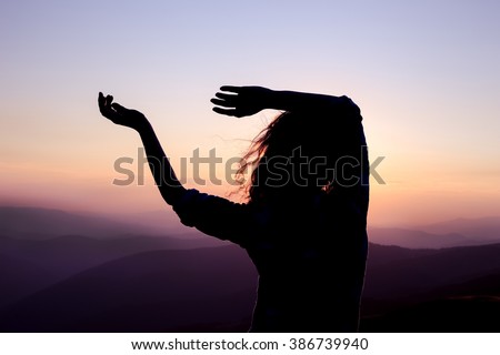 Silhouette of a young dancing woman with long wavy hair in the mountains in the backdrop of the setting sun