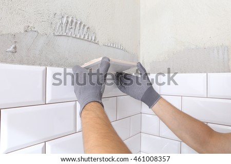 Stylish trendy white ceramic tile with a chamfer on the kitchen wall. Tiler hands in the process of laying white rectangular tiles on bathroom wall.  Repair of apartments and bathrooms.