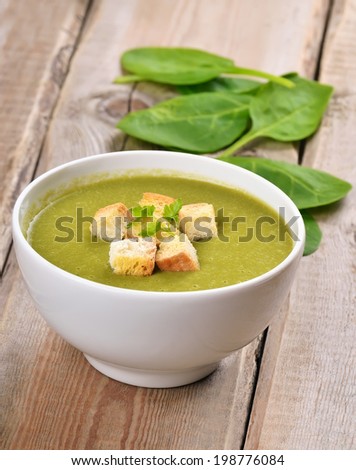 Spinach soup with dried crusts on wooden table