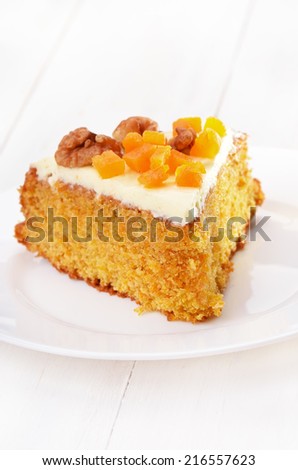 Piece of carrot cake with icing decorated dried apricots and walnut on white plate