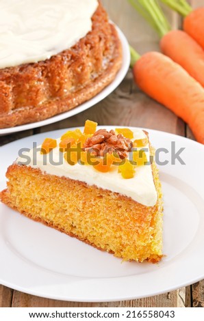 Piece of carrot cake with icing decorated dried apricots and walnut on white plate on rustic table